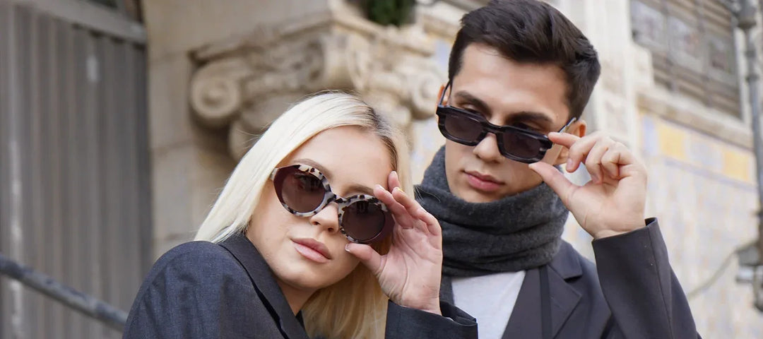 Pareja luciendo gafas de sol de diseño de la Colección Mediterránea de Acwin. Ella lleva un modelo redondo con montura carey y él unas gafas rectangulares negras estilo urbano.